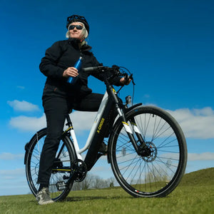 A woman taking a break on her Mark2 X-Cross 450 step-through electric bike in a sunny green park.