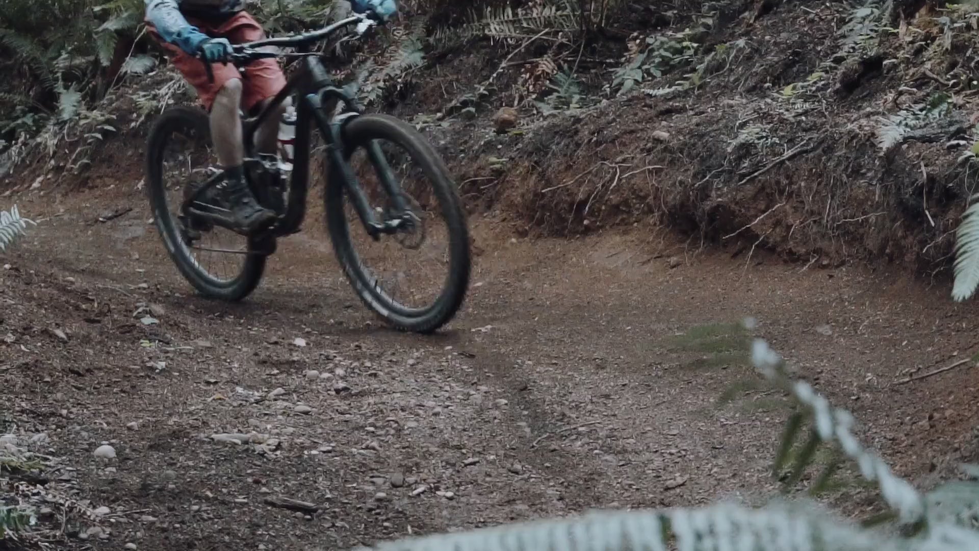 Full suspension mountain bike drifting round a corner, before blurring and the camera focusing on the foliage.