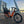 An orange Revom Multi C2 cargo e-bike with two seats and front basket, parked by a river in a city with a bridge in the background at sunset.