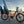 An orange Revom Multi C2 cargo e-bike with two seats and front basket, parked by a river in a city with a bridge in the background at sunset.