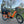 An orange Revom Multi C2 cargo e-bike with two seats and front basket, parked on a paved path in an urban area.
