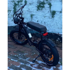 Side view of the Rocket 88X Special Edition Fat Boy electric bike with chunky Kenda off-road tyres and retro black frame, parked on brick pavement.